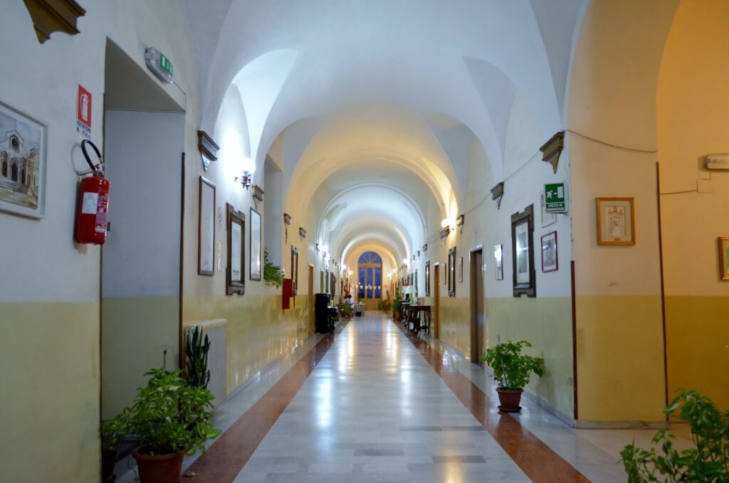 Lungo corridoio con volte, quadri e piante